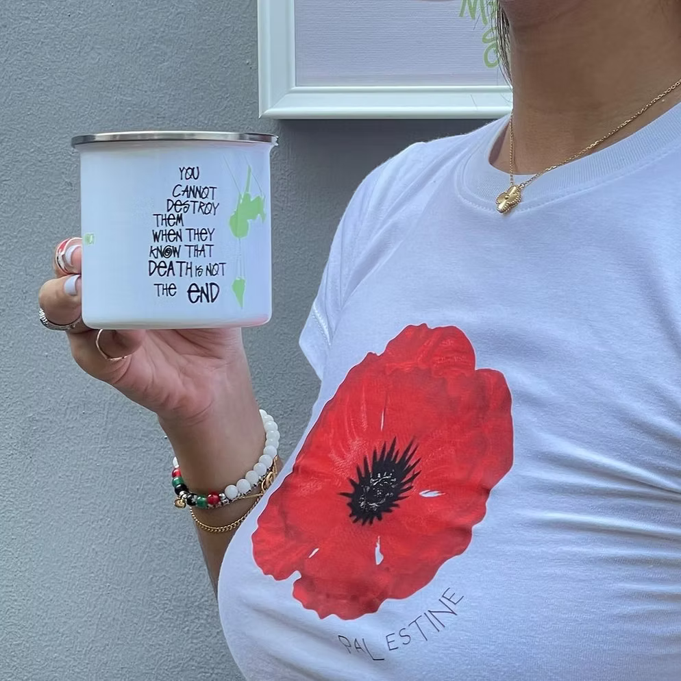 Person wearing a white t-shirt with a red floral design, holding a herblunt mug with text.